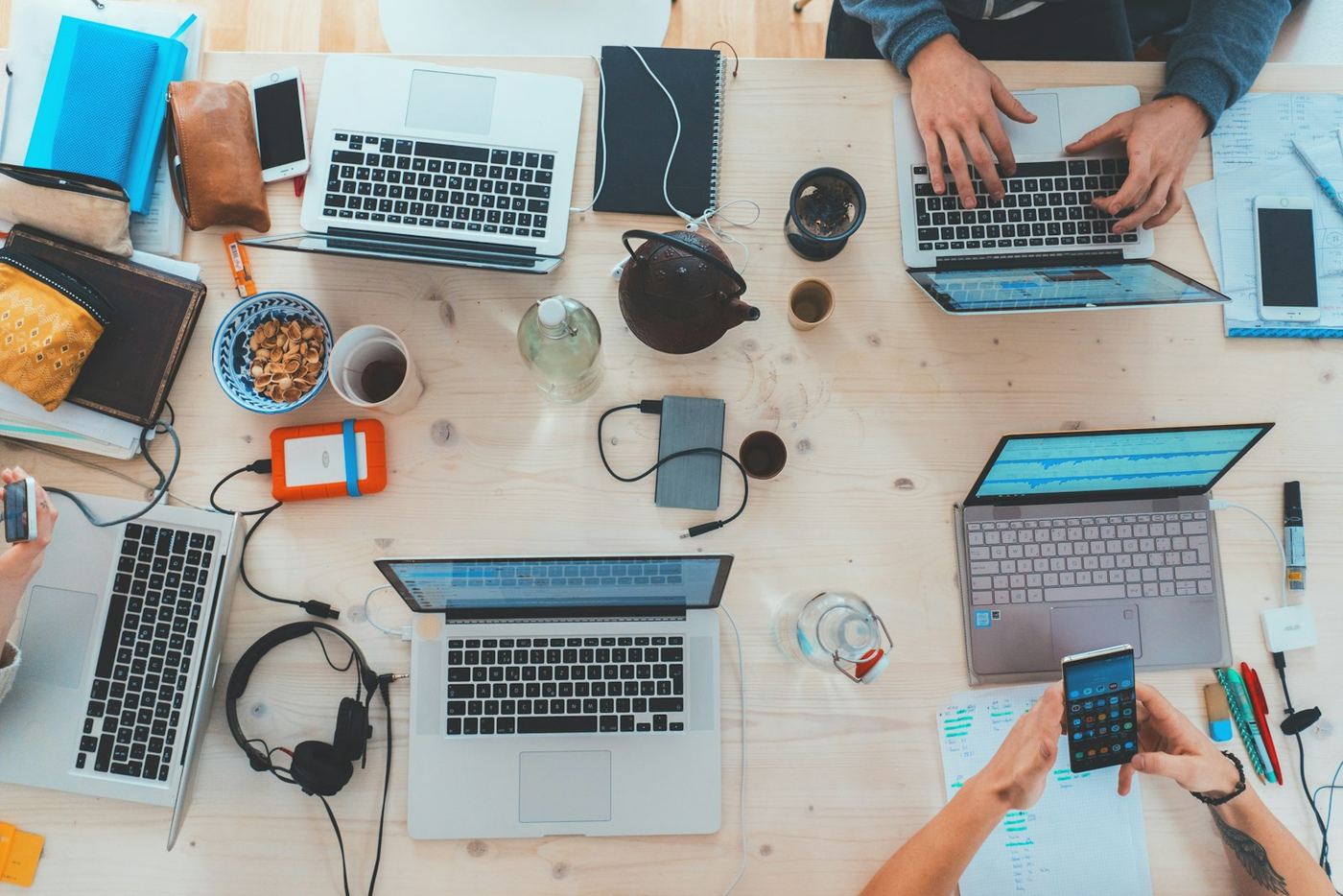 Scrivania condivisa vista dall'alto con laptop, smartphone e appunti di progetto